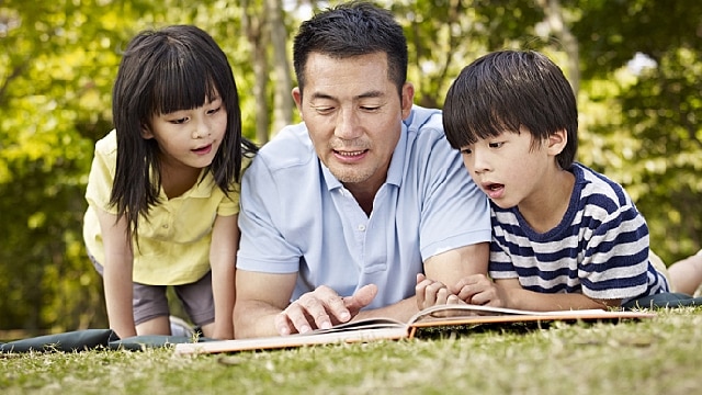 Mężczyzna z dziećmi leżą na trawie i czytają książkę