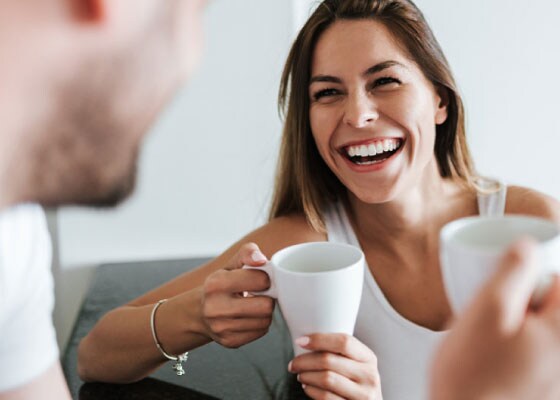 Kobieta uśmiecha się podczas rozmowy z mężczyzną trzymając kubki.