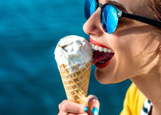 Kobieta nosząca okulary przeciwsłoneczne podczas jedzenia lodów.