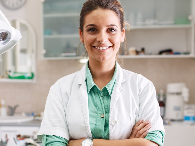 Kobieta stomatolog uśmiecha się patrząc w kamerę z założonymi rękoma.