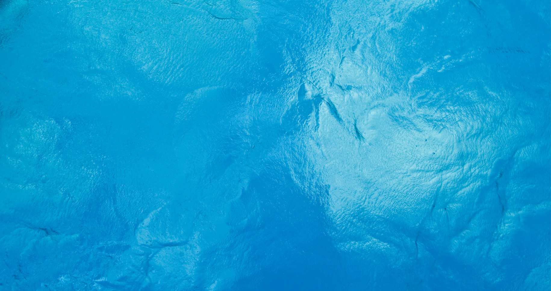 Widok z góry na błękitną tafle wody, z nieznacznymi ruchami wód