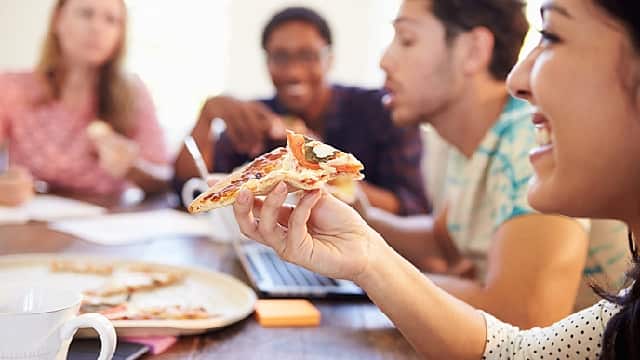 Grupa ludzi uśmiechających się i jedzących pizzę