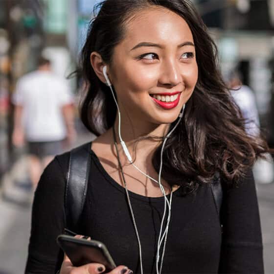 Kobieta uśmiechając się trzymając telefon ze słuchawkami.