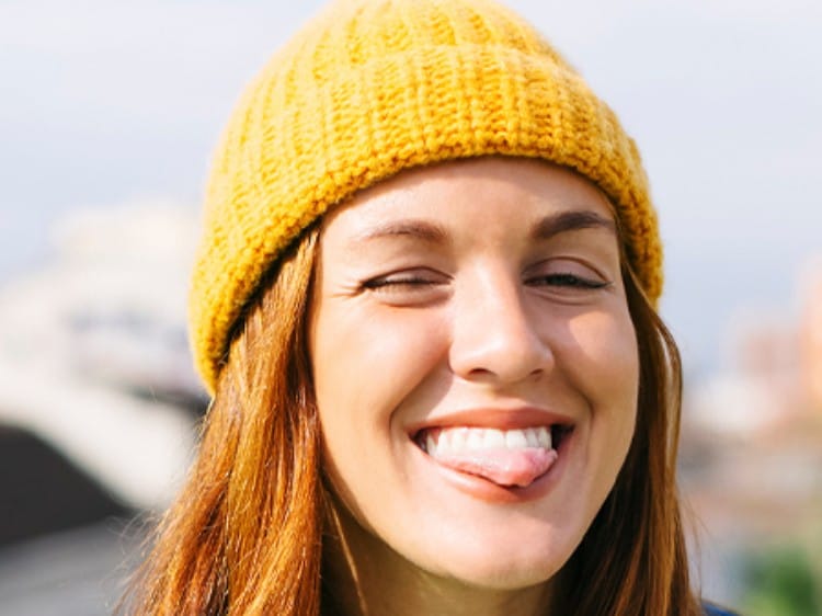 Dziewczyna w żółtej czapce z zamniętymi oczami, uśmiecha się z wyciągniętym językiem