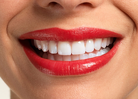 Zbliżenie na piękny, biały uśmiech kobiety z pomalowanymi na czerwono ustami.